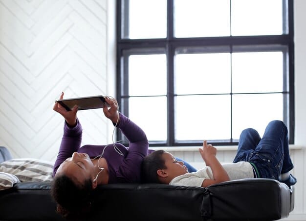 A person casually lounging on a couch with closed eyes, listening to a K-drama on a tablet, suggesting a relaxed, easy viewing experience with dubbing. The setting is cozy and inviting.